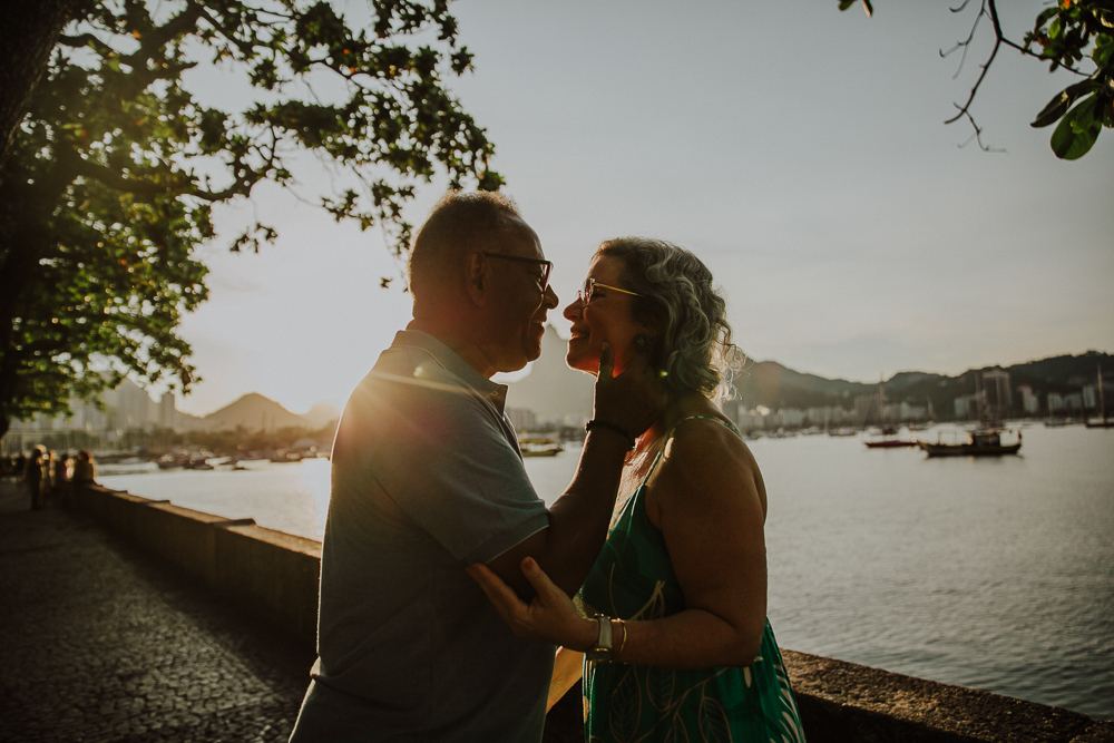  Casal maduro trocando carinho e sorrisos ao pôr do sol na Mureta da Urca, RJ.