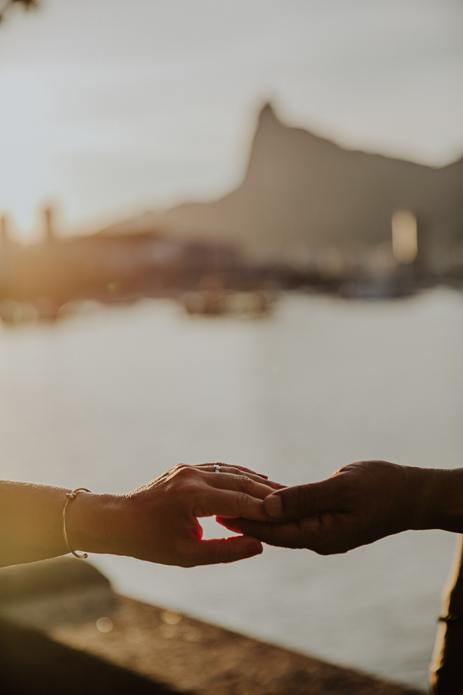  Mãos dadas de casal maduro com vista para o Pão de Açúcar ao pôr do sol no Rio de Janeiro.