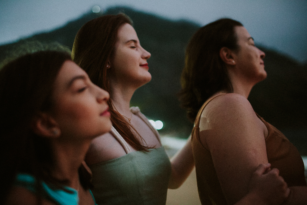 Mãe, filha e avó apreciando o pôr do sol durante ensaio de família na Praia Vermelha em um retrato poetico e cinematografico.