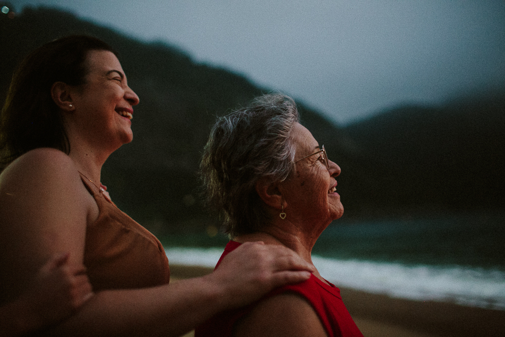 Avó sorrindo ao lado da filha em ensaio fotográfico de família na Praia Vermelha em um retrato poetico e cinematografico.