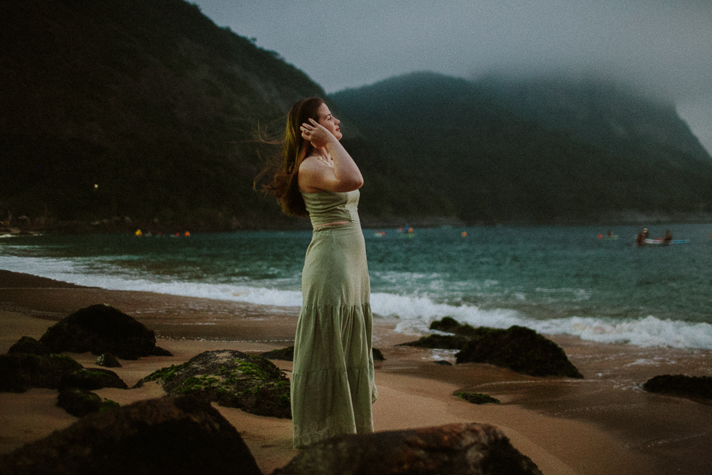 Jovem mulher caminhando pela areia durante ensaio fotográfico de família na Praia Vermelha no nascer do sol em dia nublado.