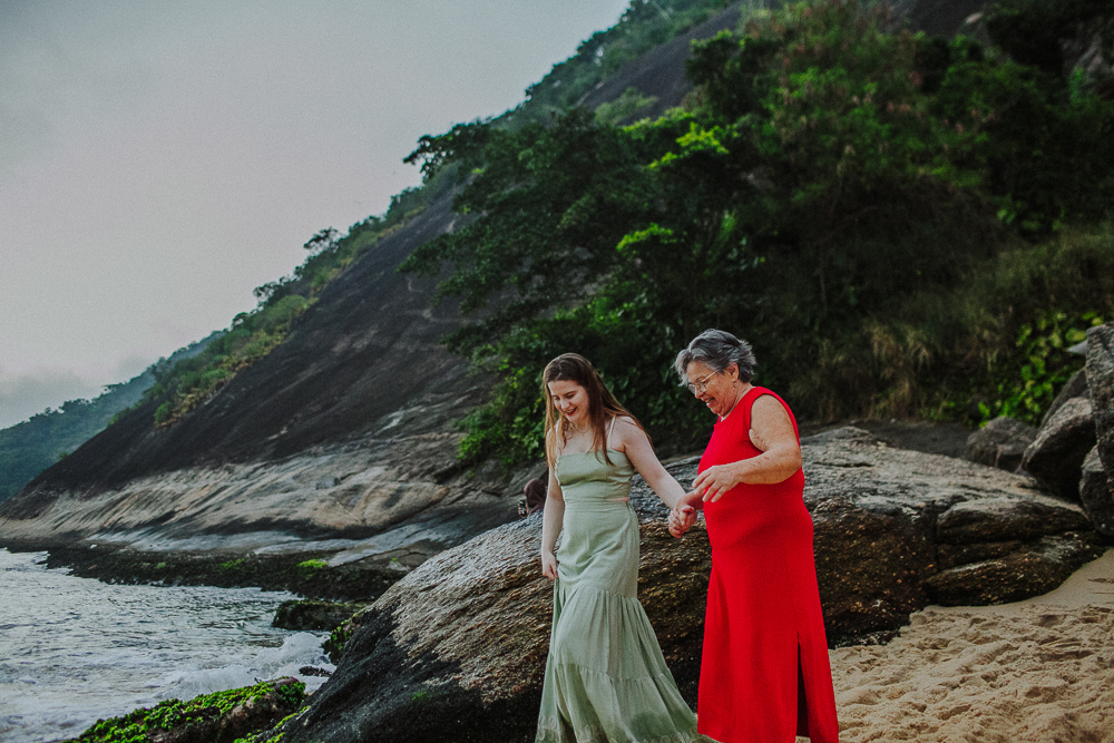 Avó e neta caminhando juntas pelas pedras da Praia Vermelha.
