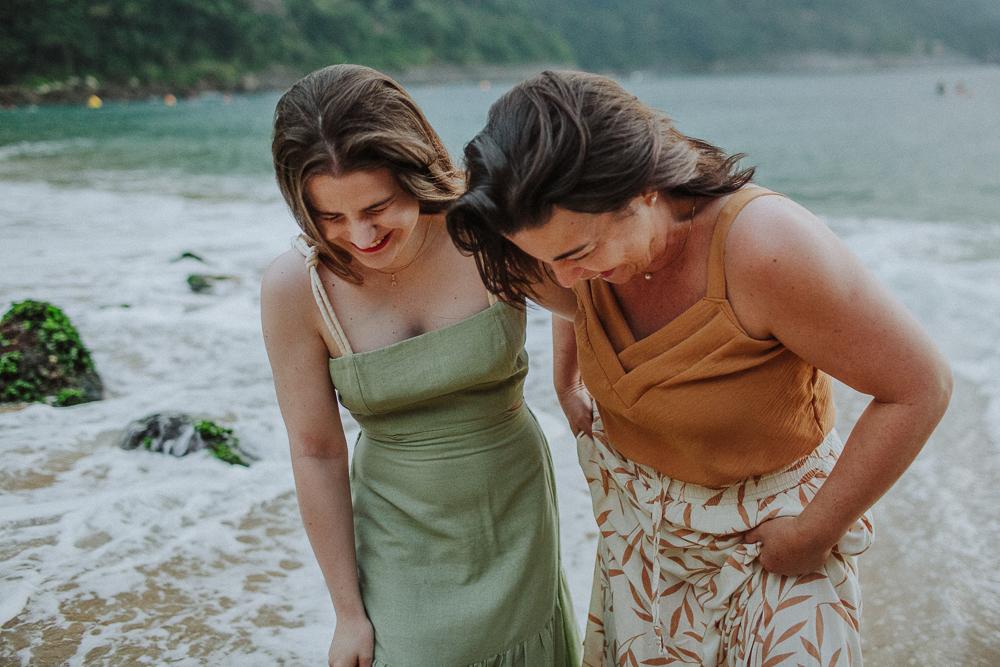 Mãe e filha caminhando e rindo espontaneamente pela água durante ensaio de família.