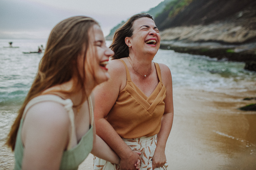 Mãe e filha de mãos dadas durante ensaio de família se divertindo e rindo muito.