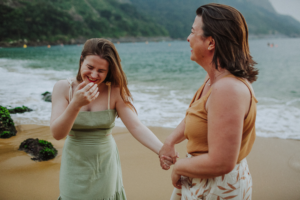 Mãe e filha de mãos dadas durante ensaio de família se divertindo e rindo muito.
