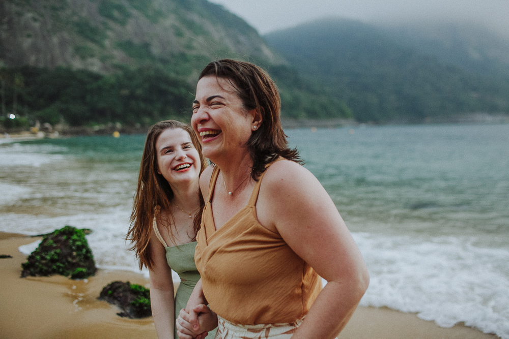 Mãe e filha de mãos dadas durante ensaio de família gargalhando.