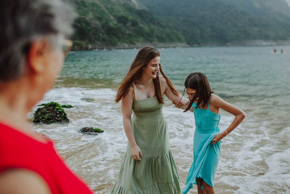 Avó observando mãe e filha brincando na praia.