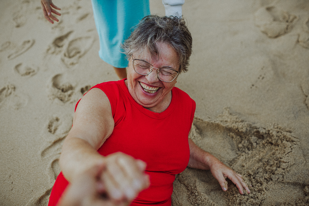 Avó rindo por ter caído sentada na areia durante ensaio na Praia Vermelha.