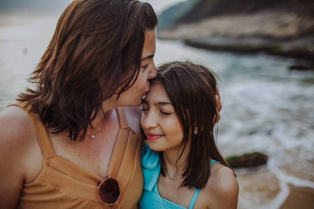 Mãe beijando a testa da filha durante ensaio de família.