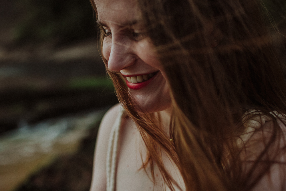 Retrato espontâneo de mulher de perfil sorrindo na praia com cabelos ao vento.