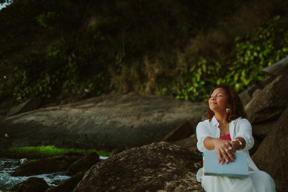 Retrato espontâneo de Alice com sua Bíblia durante ensaio de 15 anos na Praia Vermelha, Urca, com fotografia natural e afetiva.