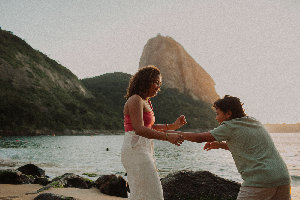 Irmãos brincando espontaneamente durante ensaio de 15 anos na Praia Vermelha, em um registro natural da relação entre eles.