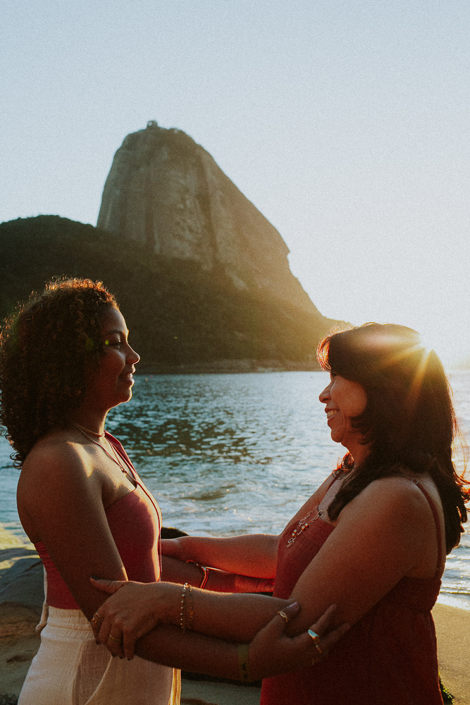 Alice e sua mãe frente a frente durante ensaio fotográfico de 15 anos na Praia Vermelha, em um momento íntimo de conexão.