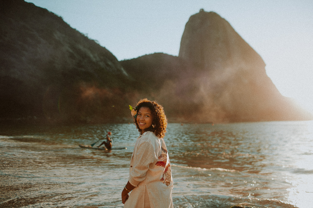 Retrato espontâneo de Alice sorrindo na Praia Vermelha durante seu ensaio fotográfico de 15 anos no Rio de Janeiro no nascer do sol
