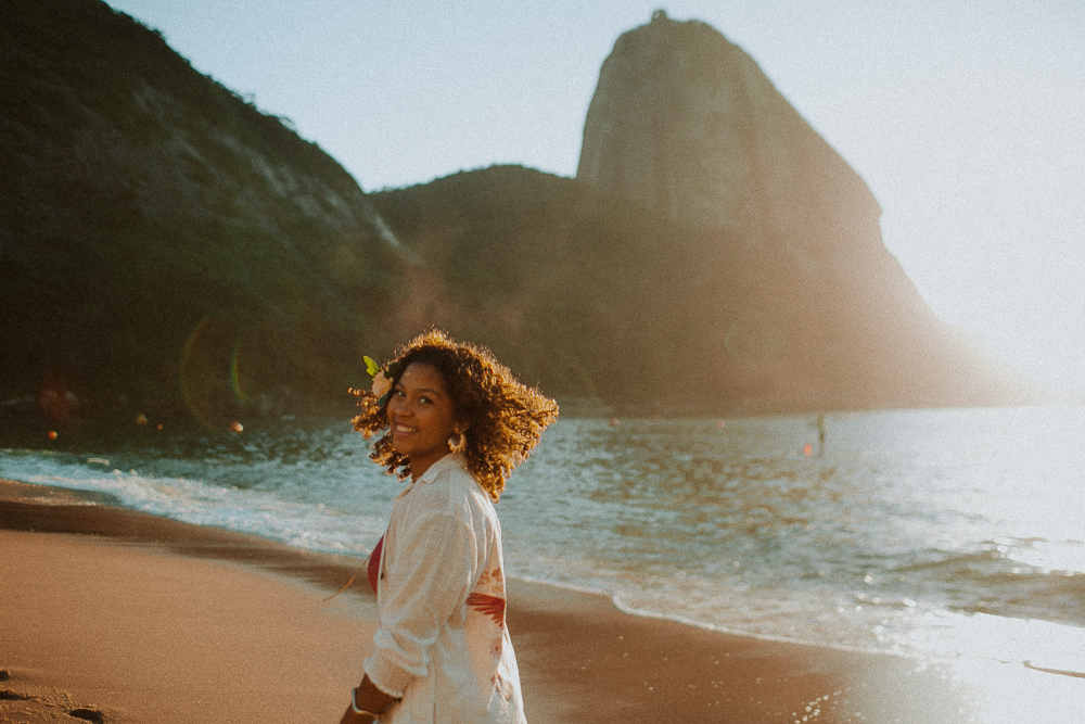 Alice sorrindo à beira-mar durante ensaio fotográfico de 15 anos na Praia Vermelha, Rio de Janeiro no nascer do sol