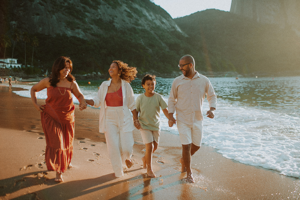 Família caminhando de mãos dadas pela Praia Vermelha durante ensaio fotográfico de 15 anos de Alice.