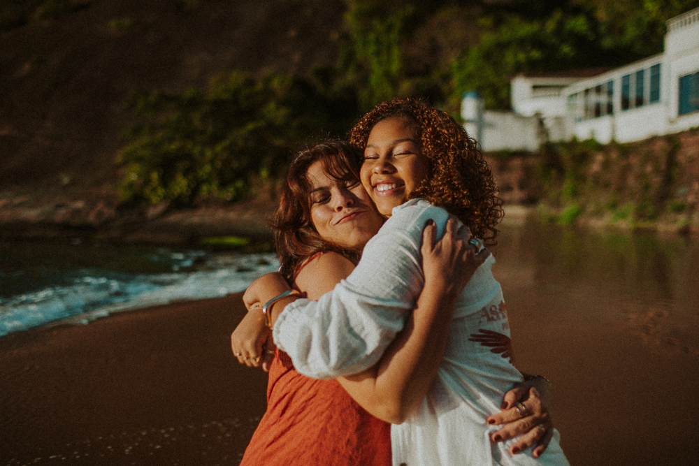 Alice e sua mãe abraçadas durante ensaio fotográfico de 15 anos na Praia Vermelha, em um registro espontâneo de afeto.