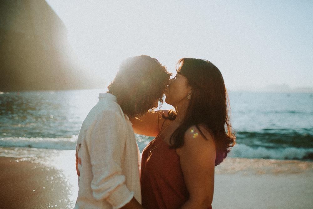 Beijo carinhoso entre Alice e sua mãe durante ensaio de 15 anos na Praia Vermelha, com o Pão de Açúcar ao fundo.