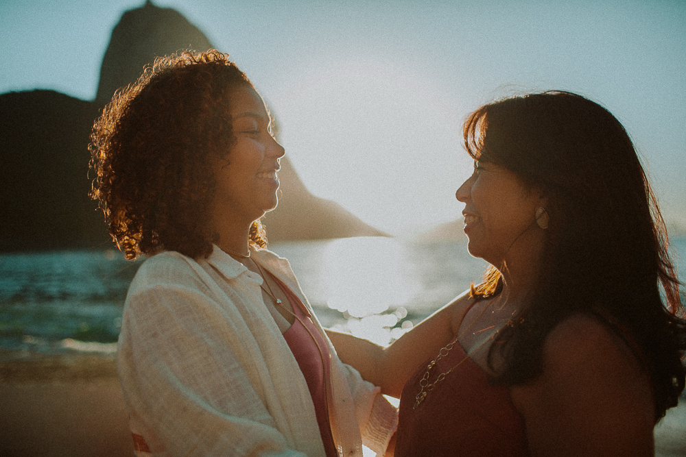 Alice e sua mãe conversando durante ensaio fotográfico de 15 anos na Praia Vermelha, em um momento natural entre mãe e filha.
