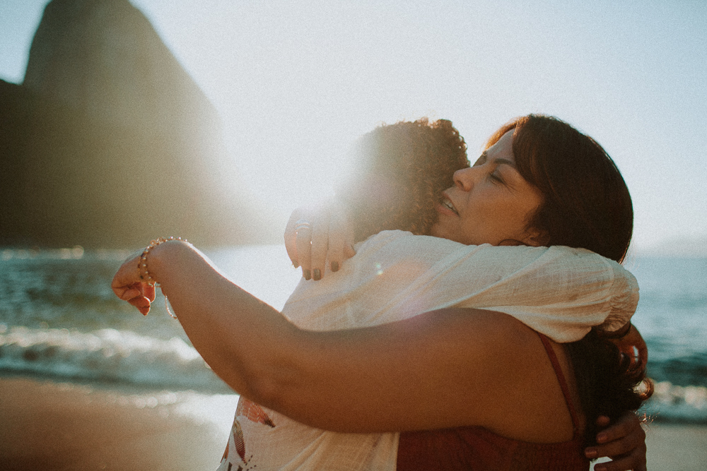 Abraço apertado e emocionado entre Alice e sua mãe durante ensaio fotográfico afetivo de 15 anos na Praia Vermelha.