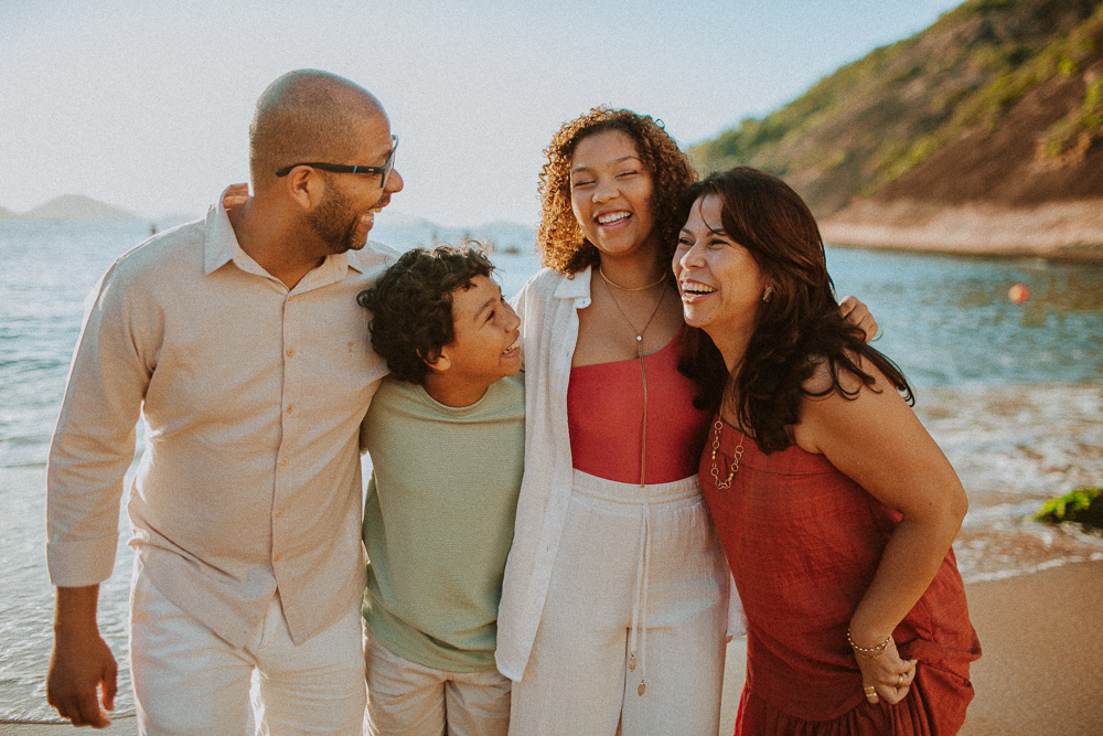 Família sorrindo junta durante ensaio fotográfico de 15 anos na Praia Vermelha, em um registro natural de conexão familiar.