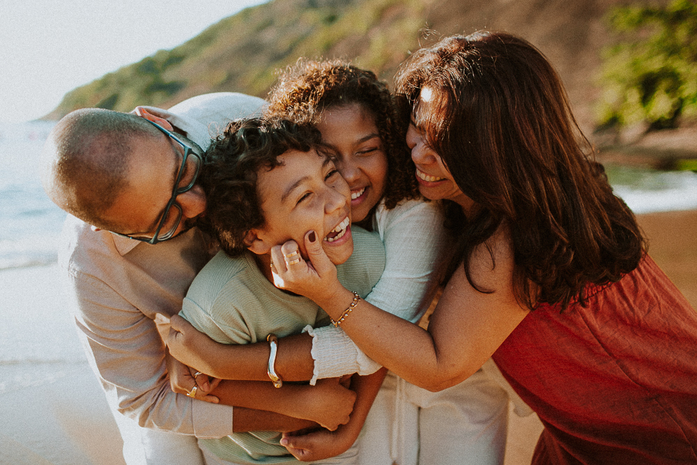 Família brincando e rindo durante ensaio fotográfico de 15 anos na Praia Vermelha, em um registro de afeto e espontaneidade.
