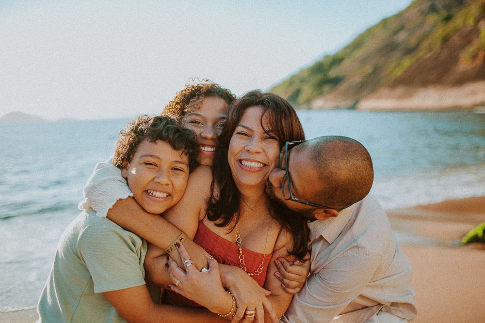 Família abraçada durante ensaio de 15 anos de Alice na Praia Vermelha, em um momento leve e cheio de afeto.
