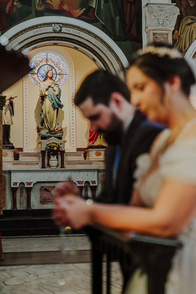 Noivos diante do altar recebendo a Eucaristia durante a celebração do Sacramento do Matrimônio em casamento católico no Grajaú, Rio de Janeiro. Fotografia de casamento por Aline Lelles do Atelier Fotografia Afetiva
