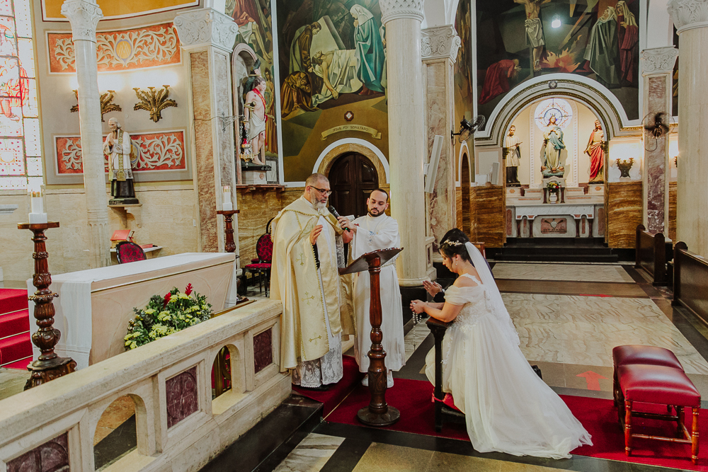 Noivos diante do altar recebendo a Eucaristia durante a celebração do Sacramento do Matrimônio em casamento católico no Grajaú, Rio de Janeiro. Fotografia de casamento por Aline Lelles do Atelier Fotografia Afetiva
