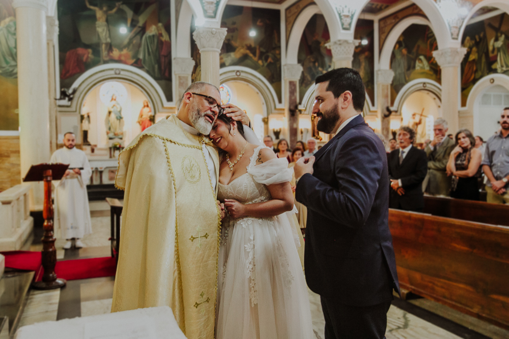 Noivos cumprimentando padre durante a celebração do Sacramento do Matrimônio em casamento católico no Grajaú, Rio de Janeiro. Fotografia de casamento por Aline Lelles do Atelier Fotografia Afetiva