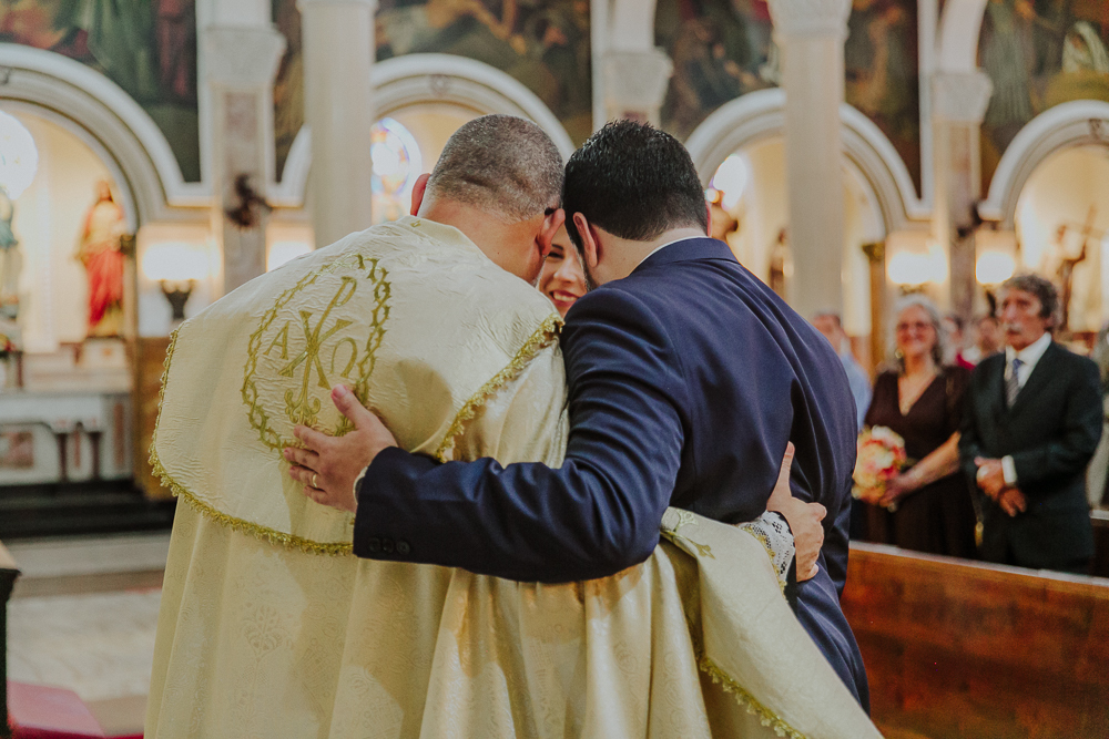 Noivos cumprimentando padre durante a celebração do Sacramento do Matrimônio em casamento católico no Grajaú, Rio de Janeiro. Fotografia de casamento por Aline Lelles do Atelier Fotografia Afetiva