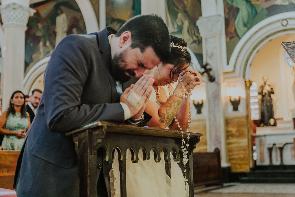 Noivos diante do altar recebendo a Eucaristia durante a celebração do Sacramento do Matrimônio em casamento católico no Grajaú, Rio de Janeiro. Fotografia de casamento por Aline Lelles do Atelier Fotografia Afetiva