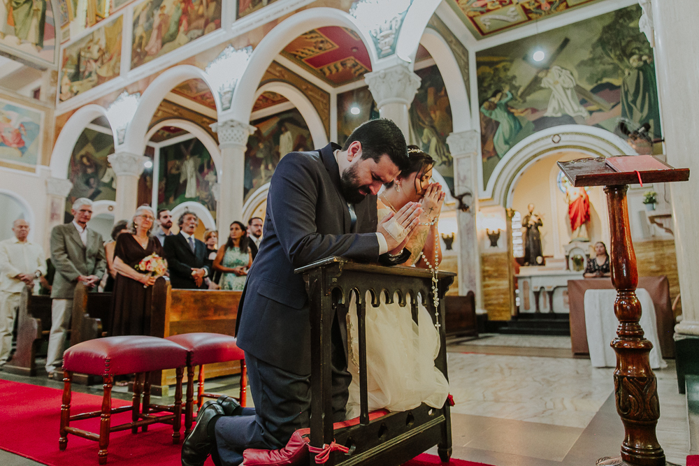 Noivos diante do altar recebendo a Eucaristia durante a celebração do Sacramento do Matrimônio em casamento católico no Grajaú, Rio de Janeiro. Fotografia de casamento por Aline Lelles do Atelier Fotografia Afetiva