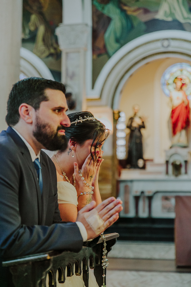 Noivos diante do altar recebendo a Eucaristia durante a celebração do Sacramento do Matrimônio em casamento católico no Grajaú, Rio de Janeiro. Fotografia de casamento por Aline Lelles do Atelier Fotografia Afetiva