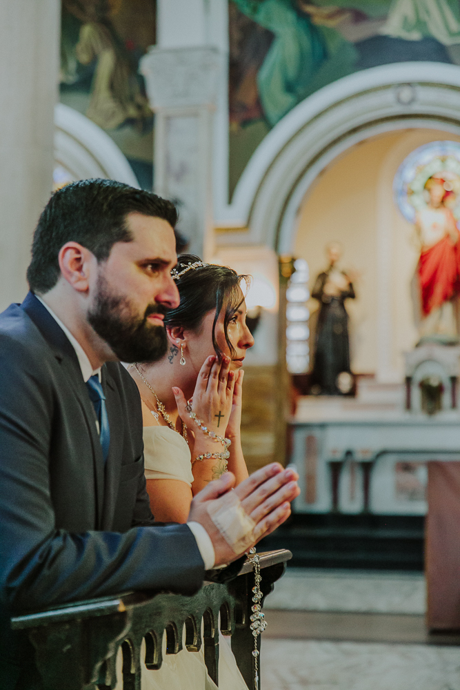 Noivos diante do altar recebendo a Eucaristia durante a celebração do Sacramento do Matrimônio em casamento católico no Grajaú, Rio de Janeiro. Fotografia de casamento por Aline Lelles do Atelier Fotografia Afetiva