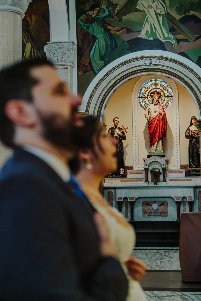 Noivos diante do altar recebendo a Eucaristia durante a celebração do Sacramento do Matrimônio em casamento católico no Grajaú, Rio de Janeiro. Fotografia de casamento por Aline Lelles do Atelier Fotografia Afetiva