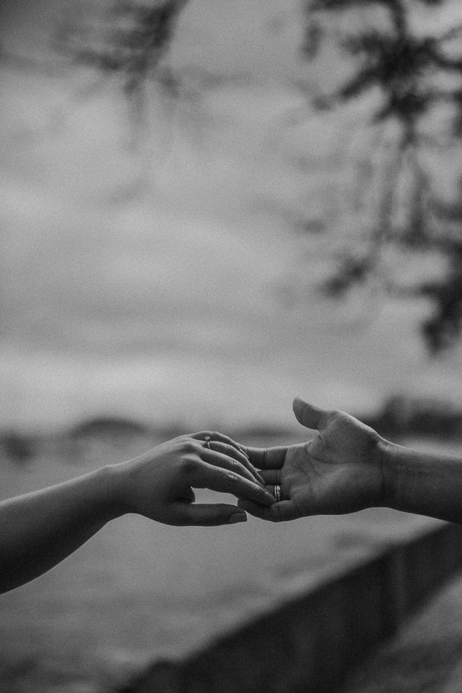 Fotografia em preto e branco das mãos do casal após o pedido de casamento na Mureta da Urca, no Rio de Janeiro, com destaque para a aliança.