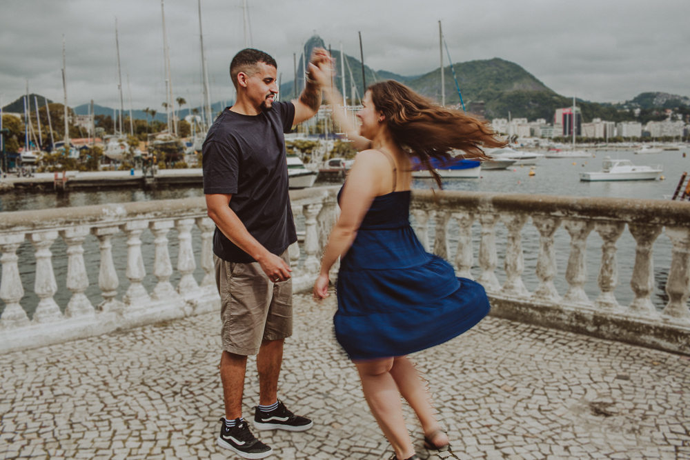 casal durante o ensaio de casal na Mureta da Urca, em uma fotografia espontânea e cheia de movimento após o pedido de casamento.