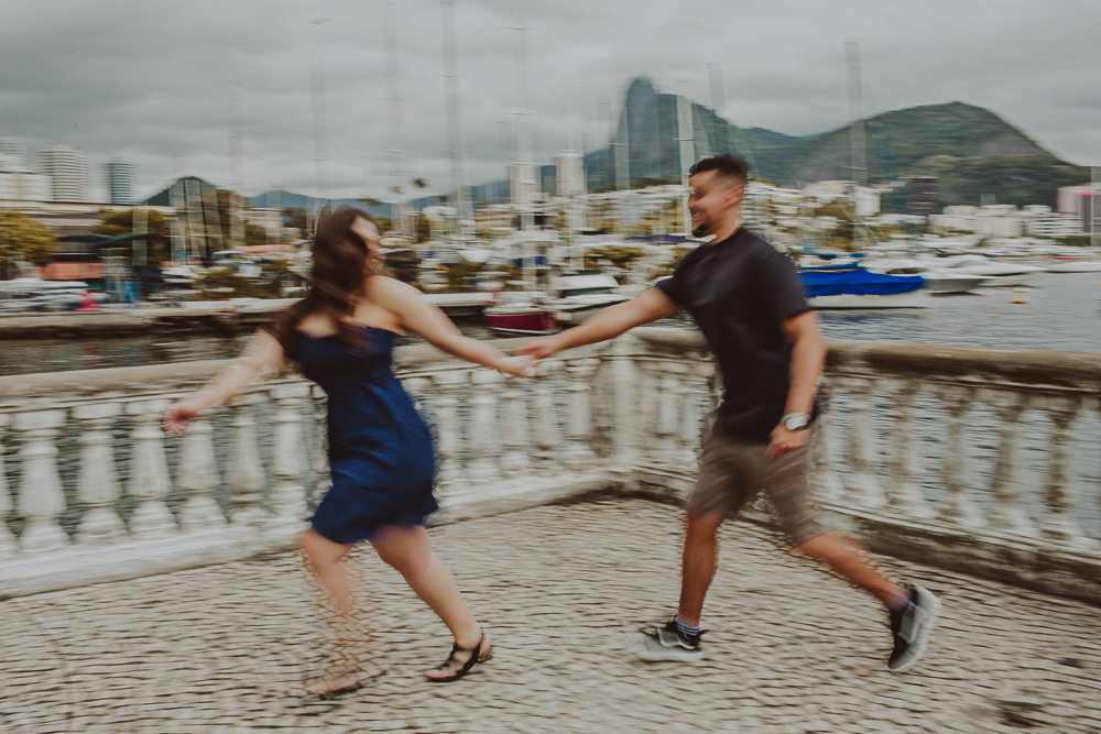 casal corre de mãos dadas pela Mureta da Urca durante o ensaio fotográfico realizado após o pedido de casamento no Rio de Janeiro.