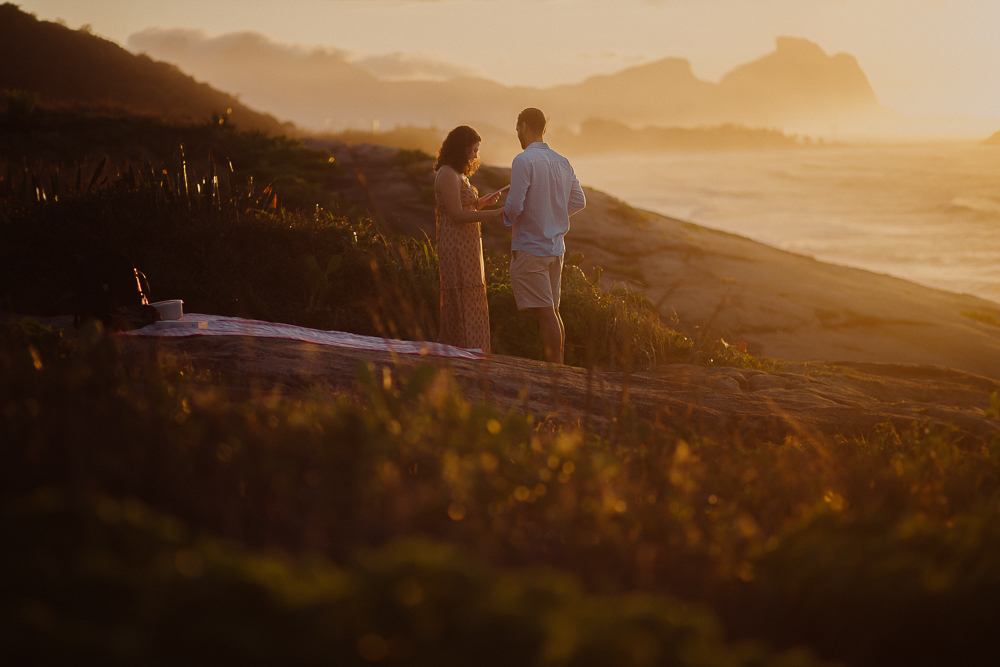 Pedido de casamento ao nascer do sol, com casal de mãos dadas sobre as pedras e o mar ao fundo, na Praia do Secreto RJ.