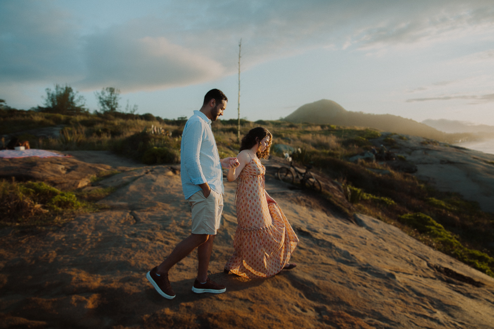 Casal caminha de mãos dadas sobre as pedras à beira-mar, aproveitando as primeiras luzes da manhã na Praia do Secreto RJ.