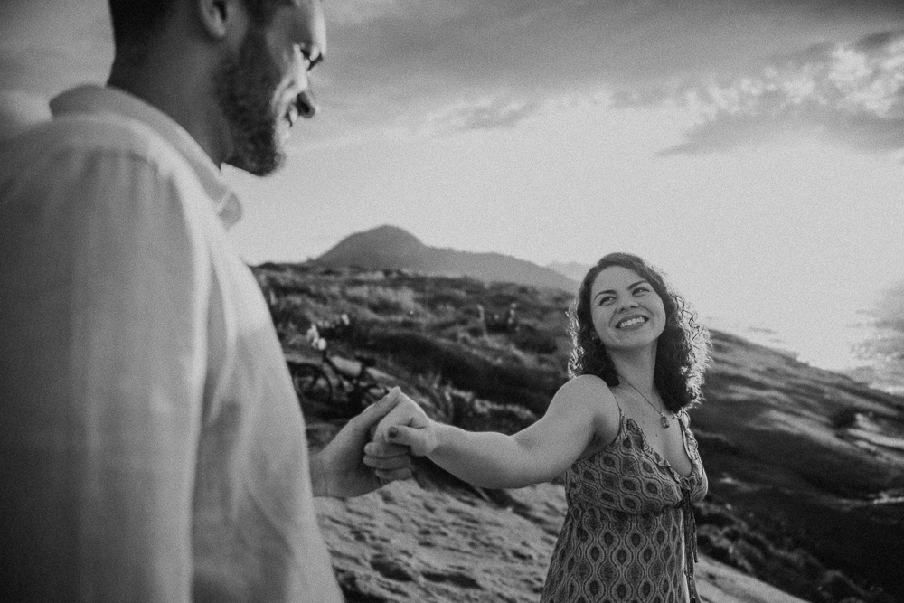Fotografia em preto e branco de mulher sorrindo enquanto segura a mão do companheiro na Praia do Secreto RJ.