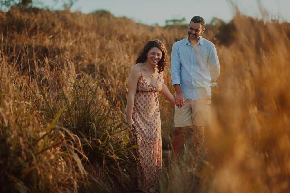 Casal passeia de mãos dadas por uma trilha de vegetação dourada durante ensaio fotográfico na Praia do Secreto RJ.
