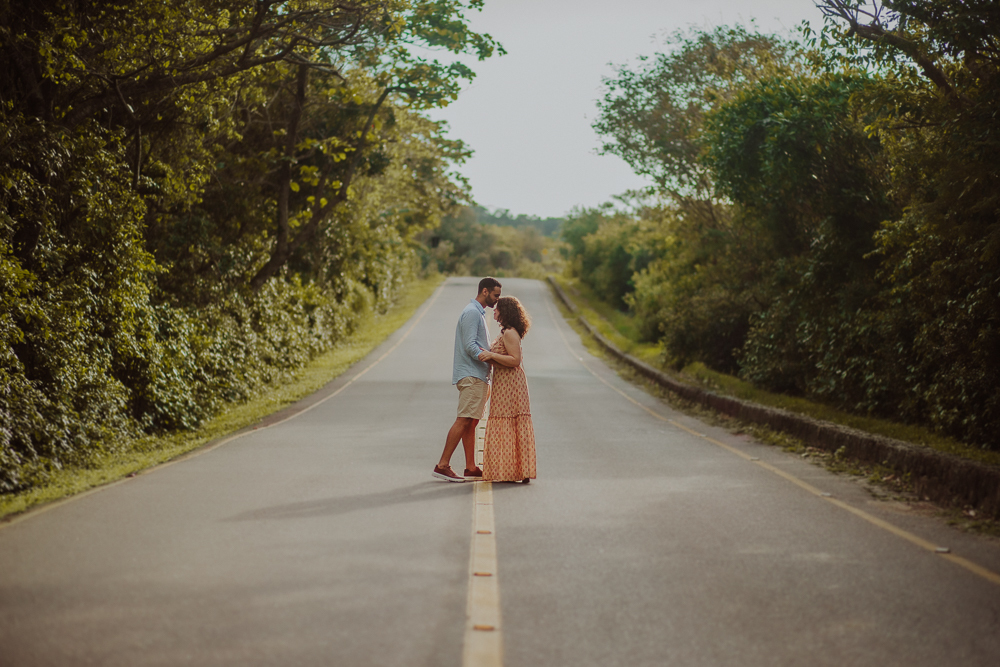 Casal se abraça no centro de uma estrada cercada por árvores, durante ensaio fotográfico na Praia do Secreto RJ.