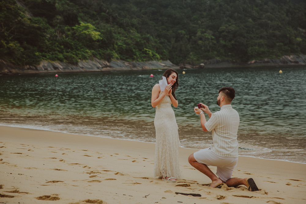 Gabriel se ajoelha diante de Júlia para fazer o pedido de casamento surpresa à beira-mar, na Praia Vermelha, Urca, Rio de Janeiro.