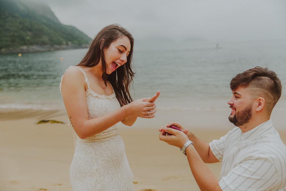 Júlia sorri enquanto admira a aliança recebida de Gabriel, em um pedido de casamento surpresa na Praia Vermelha, Rio de Janeiro.