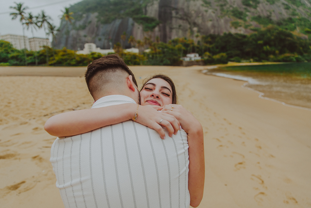 Júlia abraça Gabriel após aceitar o pedido de casamento, em um momento de emoção na areia da Praia Vermelha, Rio de Janeiro.