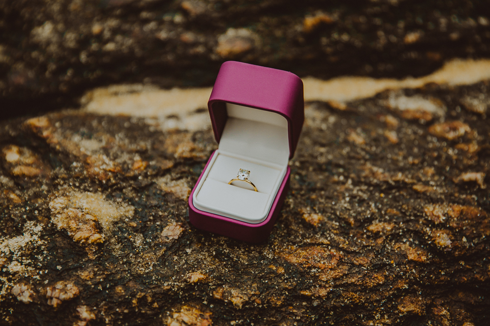Caixinha rosa aberta com anel de noivado sobre uma pedra, detalhe do pedido de casamento surpresa na Praia Vermelha, Rio de Janeiro.