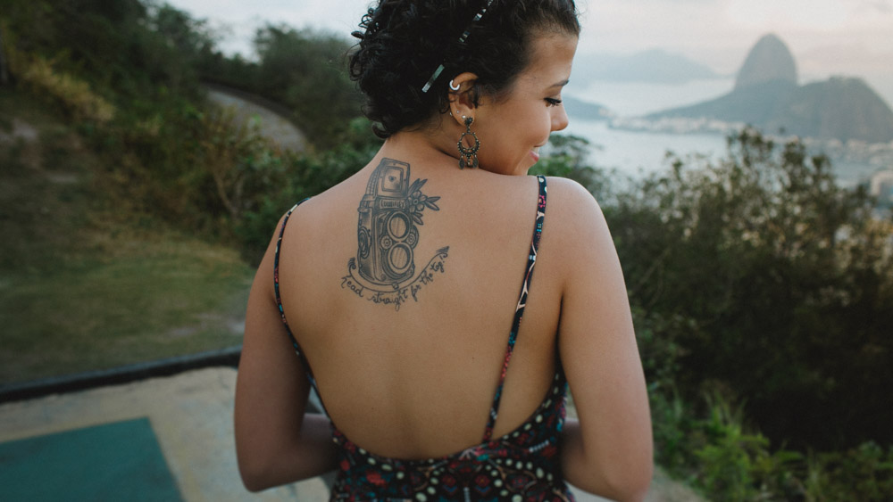 Ao fundo podemos ver o P&atilde;o de A&ccedil;&uacute;car, Nathalia posa meio t&iacute;mida e deixa revelar Tattoo feita da sua xod&oacute;, uma RolleiFlex e o texto Head straight for the top!