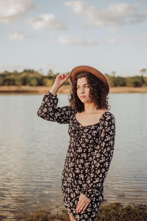 ensaio feminino externo a beira do lago com roupa preta e branca e chapeu marron estilo boho, menina cacheada